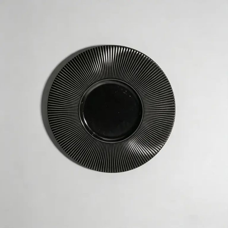 Black fluted ceramic plate with dense radial texture and glossy surface finish