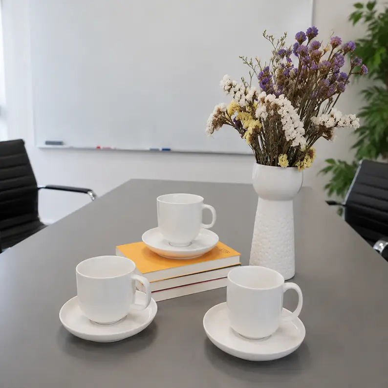Ceramic coffee cup and saucer sets arranged on a conference table for professional hospitality and office dining settings.