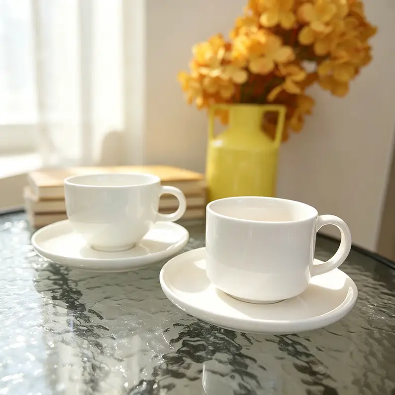 White ceramic coffee cup and saucer sets presented in a clean contemporary table setting.