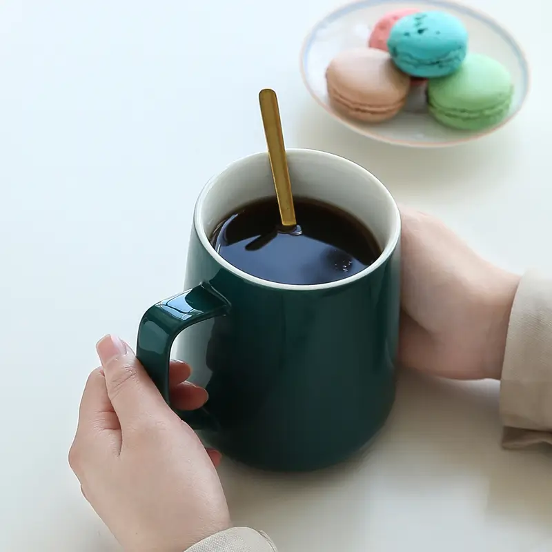 Ceramic mug with spoon held by hands showing a comfortable coffee drinking moment.